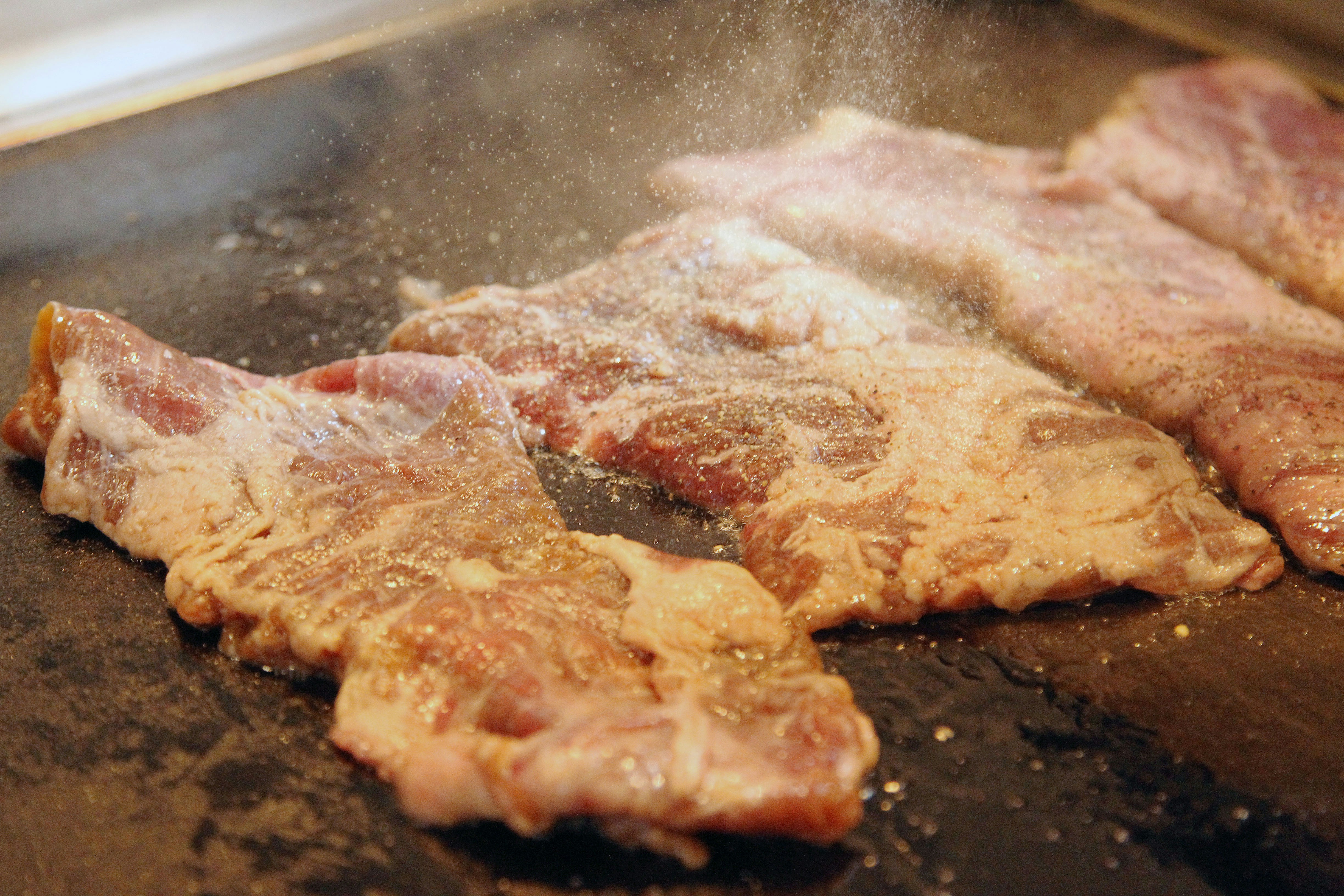 Raw meat being seasoned on a grill on commercial electric smokers.